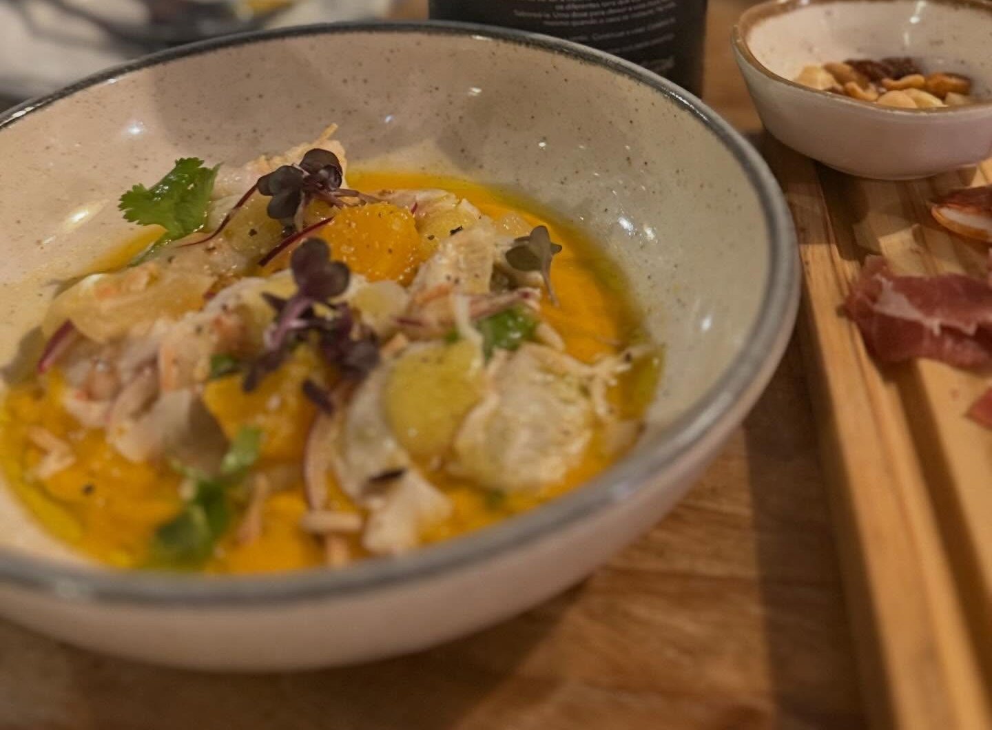 Ceviche com molho alaranjado, cebola roxa, coentros e rebentos, numa taça de cerâmica